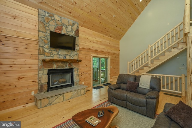 living area with wood walls, a stone fireplace, wood finished floors, high vaulted ceiling, and stairs