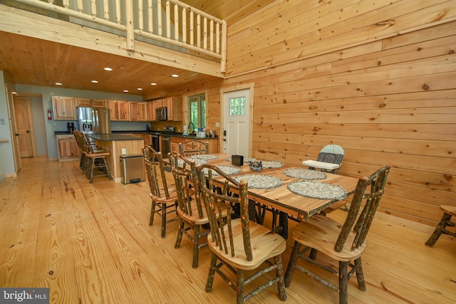 dining space featuring light wood-type flooring, wooden walls, a towering ceiling, and recessed lighting