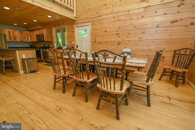 dining space with wood walls, recessed lighting, and light wood-style floors