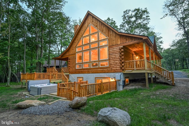 rear view of house featuring a deck, stairs, log exterior, a chimney, and a hot tub