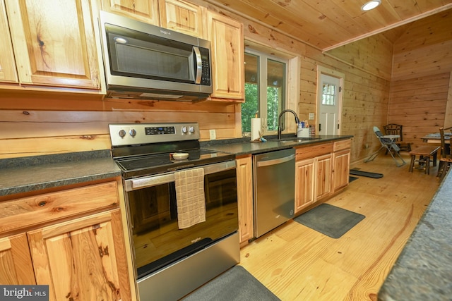 kitchen with stainless steel appliances, dark countertops, wood ceiling, a sink, and wood walls