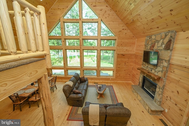 living room with wood ceiling, wood finished floors, a stone fireplace, wood walls, and high vaulted ceiling