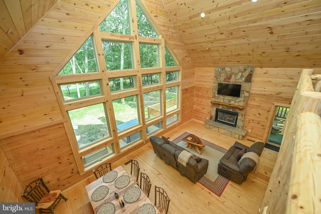 living room with wood walls, high vaulted ceiling, wood finished floors, and a stone fireplace