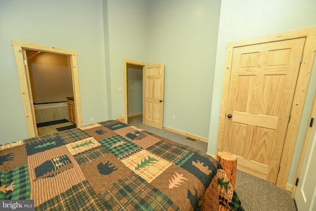 unfurnished bedroom with ensuite bathroom, carpet, a towering ceiling, and baseboards