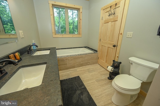 bathroom with a garden tub, wood finished floors, a sink, and toilet