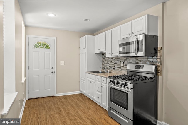 kitchen with stainless steel appliances, sink, white cabinets, light hardwood / wood-style flooring, and decorative backsplash