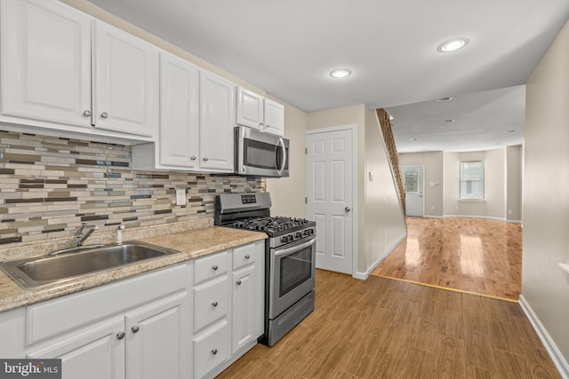 kitchen featuring appliances with stainless steel finishes, light wood-type flooring, sink, tasteful backsplash, and white cabinetry