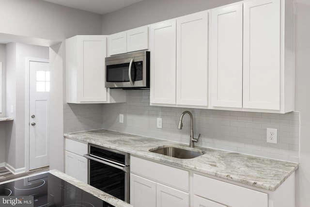 kitchen with appliances with stainless steel finishes, decorative backsplash, sink, and white cabinets