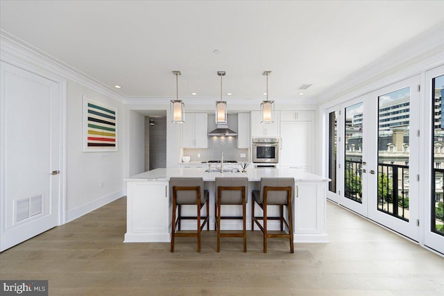 kitchen featuring white cabinetry, oven, french doors, a kitchen island with sink, and wall chimney range hood