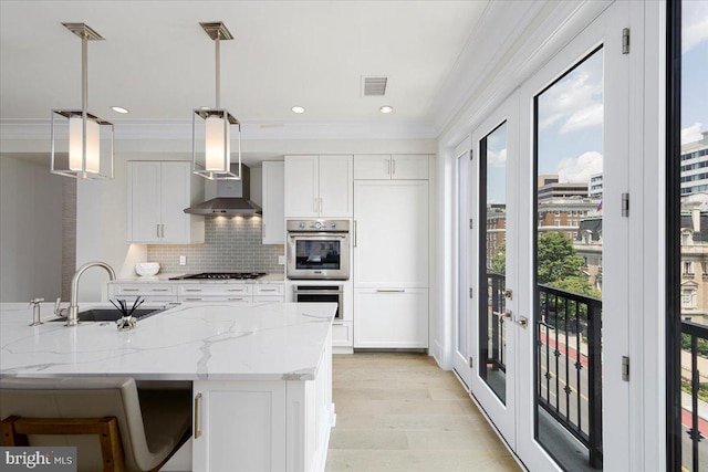 kitchen with wall chimney range hood, decorative light fixtures, white cabinets, and a wealth of natural light