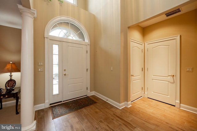 entryway with a high ceiling, a healthy amount of sunlight, ornate columns, and hardwood / wood-style floors