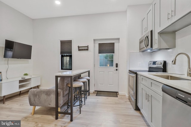 kitchen featuring light stone counters, appliances with stainless steel finishes, backsplash, light wood-type flooring, and sink