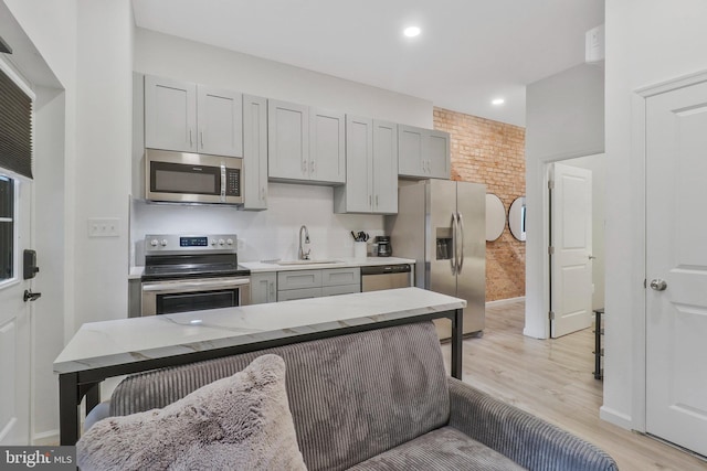 kitchen featuring light wood-type flooring, gray cabinets, stainless steel appliances, light stone counters, and sink