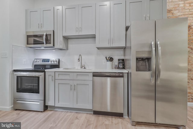 kitchen with gray cabinets, light hardwood / wood-style floors, backsplash, stainless steel appliances, and sink