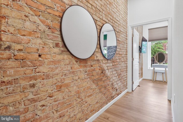 corridor with light wood-type flooring and brick wall