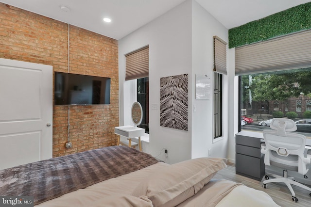 bedroom with light wood-type flooring and brick wall