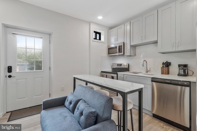 kitchen with tasteful backsplash, sink, stainless steel appliances, and light hardwood / wood-style flooring