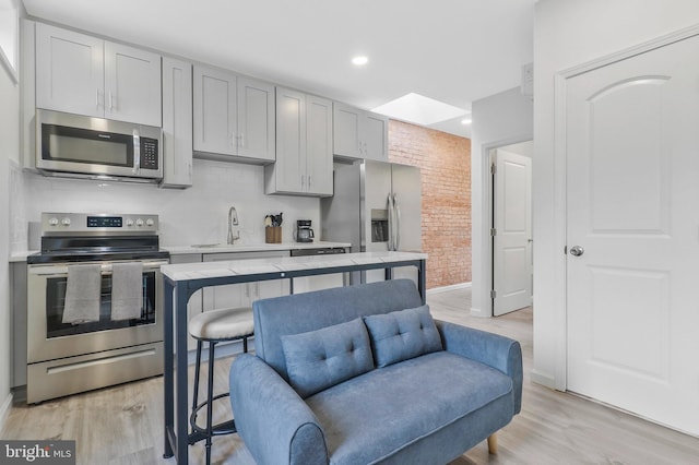 kitchen featuring brick wall, stainless steel appliances, sink, and light hardwood / wood-style floors