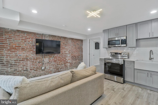 kitchen with appliances with stainless steel finishes, gray cabinets, sink, and light hardwood / wood-style floors