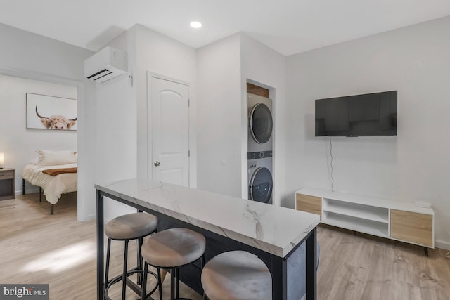 kitchen featuring light wood-type flooring, a breakfast bar, stacked washer and dryer, a wall mounted AC, and light stone counters