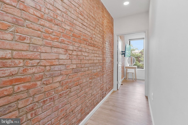 corridor with light hardwood / wood-style flooring and brick wall