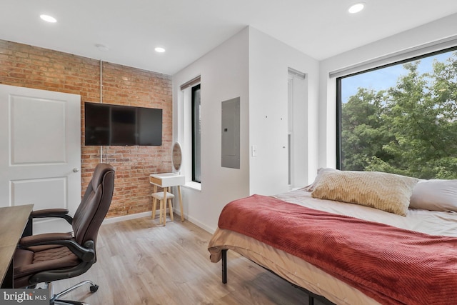 bedroom with light wood-type flooring, brick wall, and electric panel