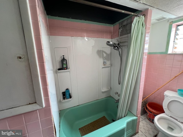 bathroom featuring toilet, shower / bathtub combination with curtain, wainscoting, visible vents, and tile walls