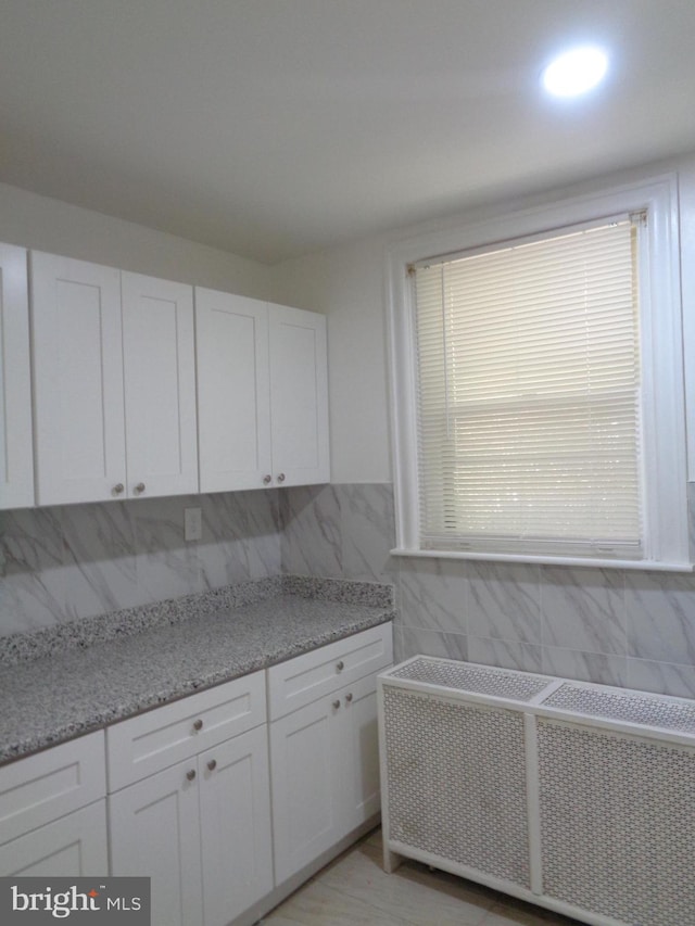 kitchen with tasteful backsplash, light stone counters, and white cabinetry