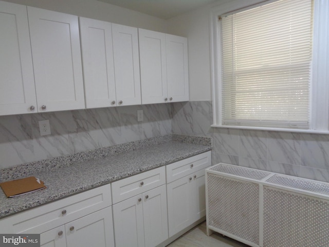 kitchen with decorative backsplash, light stone countertops, and white cabinetry