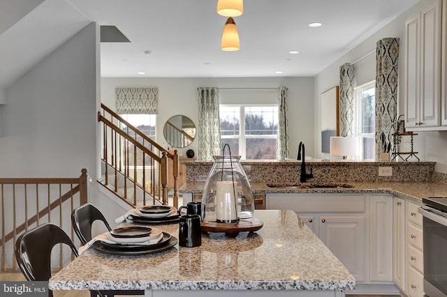 kitchen with pendant lighting, light stone countertops, sink, and white cabinets