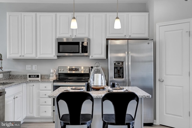 kitchen with pendant lighting, appliances with stainless steel finishes, light stone counters, and white cabinets