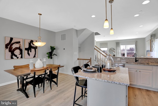 kitchen with sink, light stone counters, white cabinetry, hanging light fixtures, and light hardwood / wood-style flooring