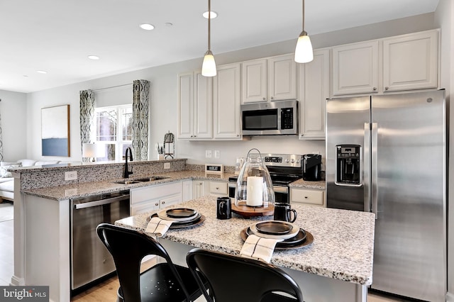 kitchen with sink, white cabinetry, stainless steel appliances, a kitchen breakfast bar, and decorative light fixtures