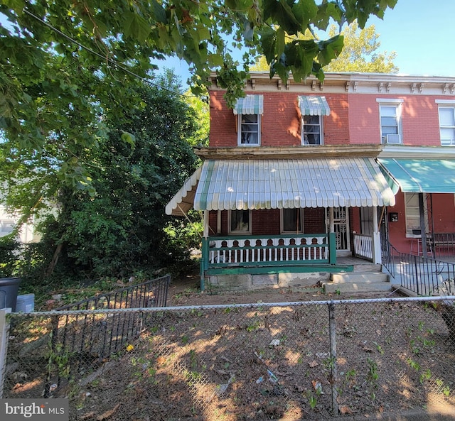 view of front of home with covered porch, brick siding, and a fenced front yard