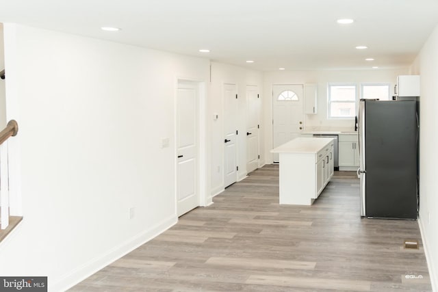 kitchen with appliances with stainless steel finishes, a kitchen island, sink, light hardwood / wood-style floors, and white cabinetry