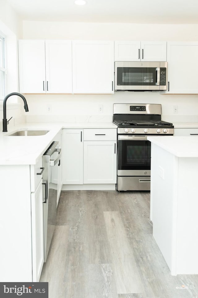 kitchen with white cabinets, sink, stainless steel appliances, and light hardwood / wood-style flooring