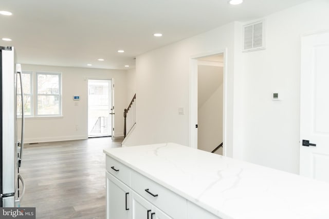 kitchen with white cabinets, hardwood / wood-style floors, white fridge, and light stone countertops