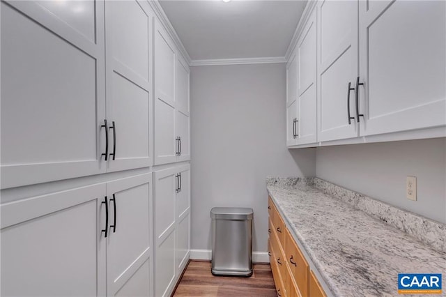 kitchen featuring light stone counters, ornamental molding, hardwood / wood-style floors, and white cabinetry