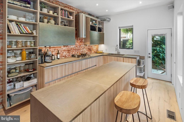 kitchen featuring sink, a center island, light brown cabinetry, light hardwood / wood-style floors, and stainless steel gas stovetop