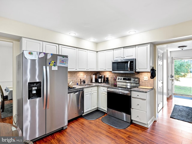 kitchen featuring appliances with stainless steel finishes, decorative backsplash, white cabinets, and hardwood / wood-style floors