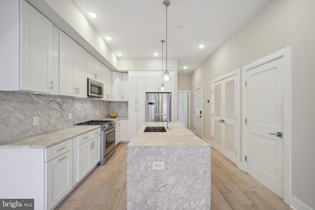 kitchen featuring stainless steel appliances, a kitchen island with sink, hanging light fixtures, and white cabinets