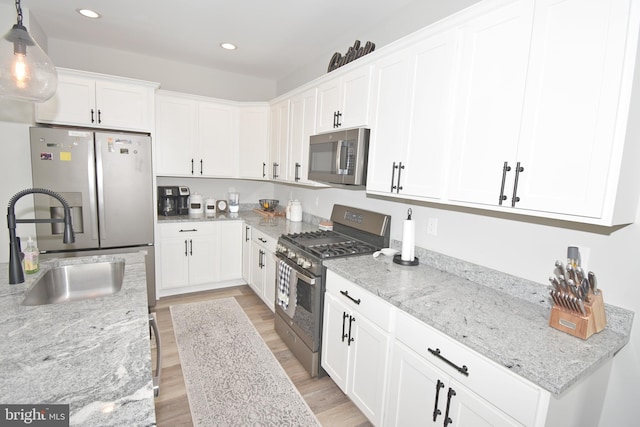 kitchen with appliances with stainless steel finishes, light wood-type flooring, light stone counters, white cabinets, and hanging light fixtures