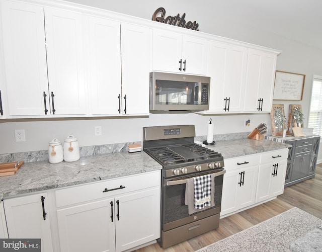 kitchen featuring light stone countertops, light wood-type flooring, stainless steel appliances, and white cabinetry