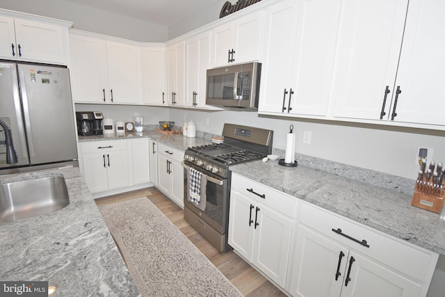 kitchen with white cabinets, light stone counters, stainless steel appliances, and light hardwood / wood-style flooring