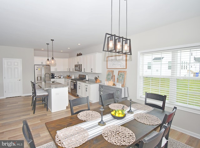 dining room with a wealth of natural light, sink, a notable chandelier, and light hardwood / wood-style flooring