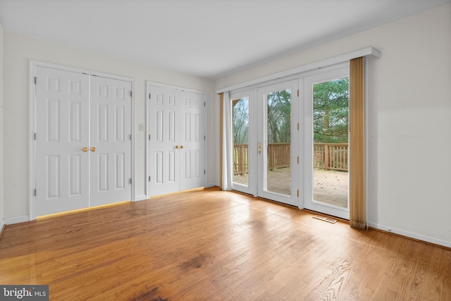 unfurnished bedroom with light hardwood / wood-style floors, french doors, access to outside, and multiple closets