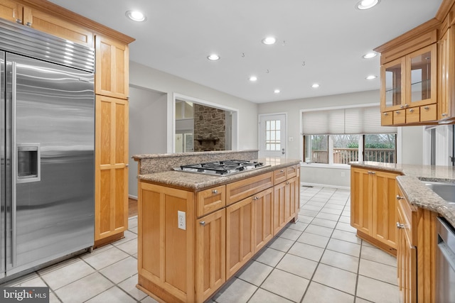 kitchen featuring a stone fireplace, light stone countertops, light tile patterned floors, a kitchen island, and stainless steel appliances