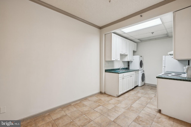 kitchen featuring a drop ceiling, stacked washing maching and dryer, white cabinets, light tile patterned floors, and sink