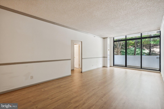 empty room featuring a textured ceiling, light hardwood / wood-style floors, a wall of windows, and ornamental molding