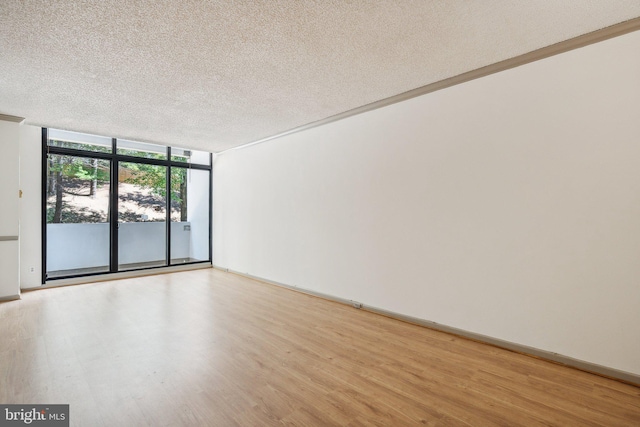 unfurnished room with light wood-type flooring, ornamental molding, a textured ceiling, and floor to ceiling windows